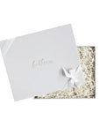 Light grey box with foxblossom.co embossed with gold foil, filled with white paper shred and  tied with white ribbon. 