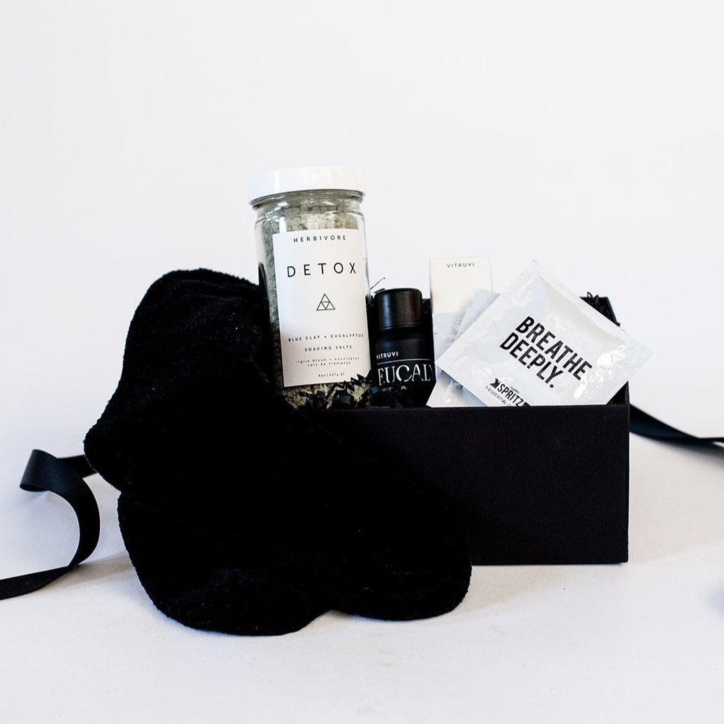 Black chenille socks, Herbivore detox bath salts, vitruvi eucalyptus essential oil, Spritz breathe deeply set of three wipes in a black box.