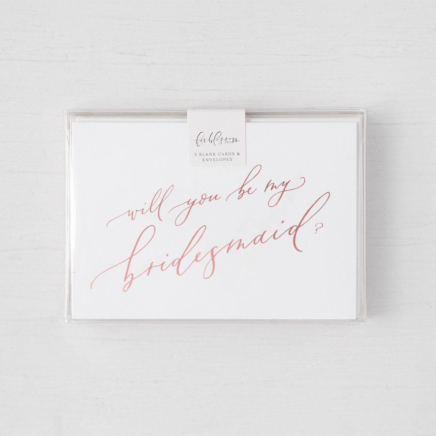 White envelope size card (approx. 3.5&quot; x 5&quot;), reads, &quot;Will you be my bridesmaid?&quot; in rose gold text in a clear plastic bag,