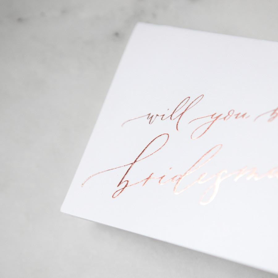 White envelope size card (approx. 3.5&quot; x 5&quot;), reads, &quot;Will you be my bridesmaid?&quot; in rose gold text zoomed in.