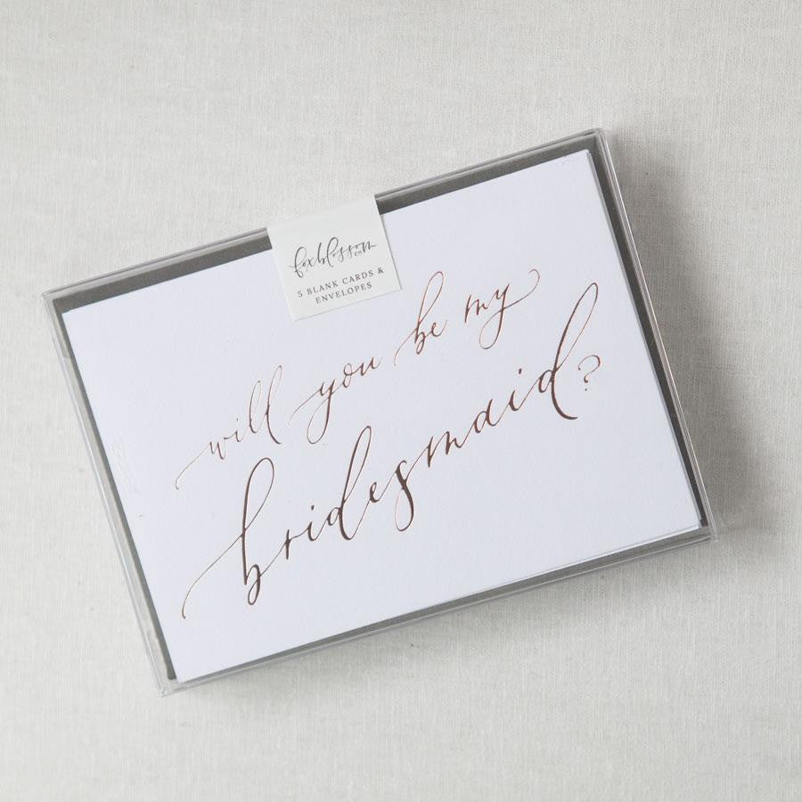 White envelope size card (approx. 3.5&quot; x 5&quot;), reads, &quot;Will you be my bridesmaid?&quot; in rose gold text in a clear plastic bag.