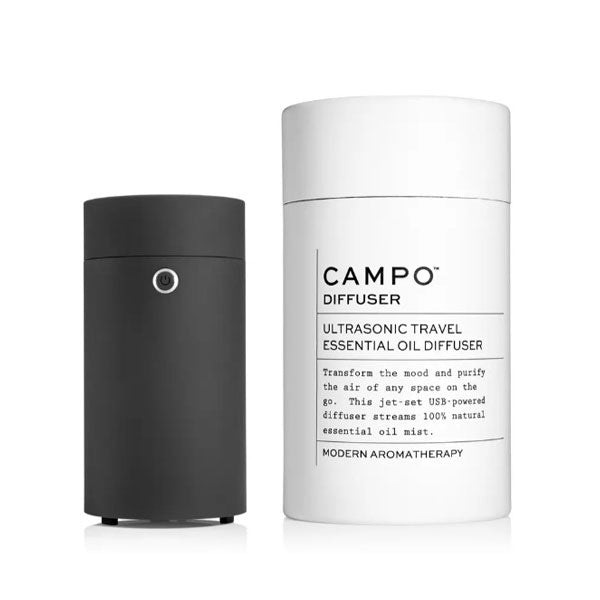 Black Campo diffuser shown next to white container tube which read &quot;Campo diffuser, ultrasonic travel essential oil diffuser. Transform teh mood and purify the air of any space on the go. This jet-set USB-powered diffuser streams 100% natural essential oil mist. Modern aromatherapy. &quot;