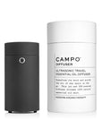 Black Campo diffuser shown next to white container tube which read "Campo diffuser, ultrasonic travel essential oil diffuser. Transform teh mood and purify the air of any space on the go. This jet-set USB-powered diffuser streams 100% natural essential oil mist. Modern aromatherapy. "