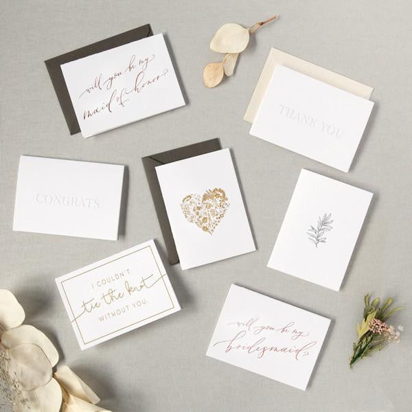 Seven car options, and floral bundles/flower stems. some read, &quot;will you be my maid of honor?&quot;, &quot;Congrats&quot;, &quot;I couldn&#39;t tie the knot without you&quot;, &quot;thank you&quot;, and will you be my bridesmaid?&quot;. Others have a golden heart and floral graphics. A few paired with envelope color options: slate gray or ivory shimmer.