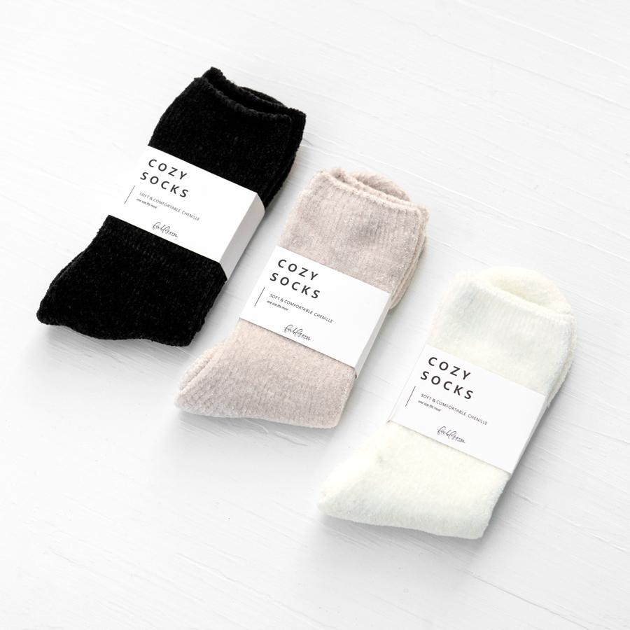 Three pairs of chenille socks. Black, nude, and ivory color options. Each has a white band around the center that reads "Cozy Socks"