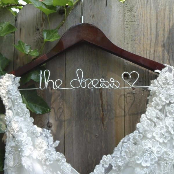 Dark brown wooden hanger with silver hook. Silver wire base shaped to read "the dress"