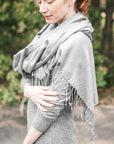 Woman in an outdoor setting, wearing a grey dress and draped with a grey pashmina. 