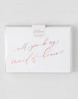 White envelope size card (approx. 3.5" x 5"), reads, "Will you be my maid of honor?" in rose gold text in a clear plastic bag.