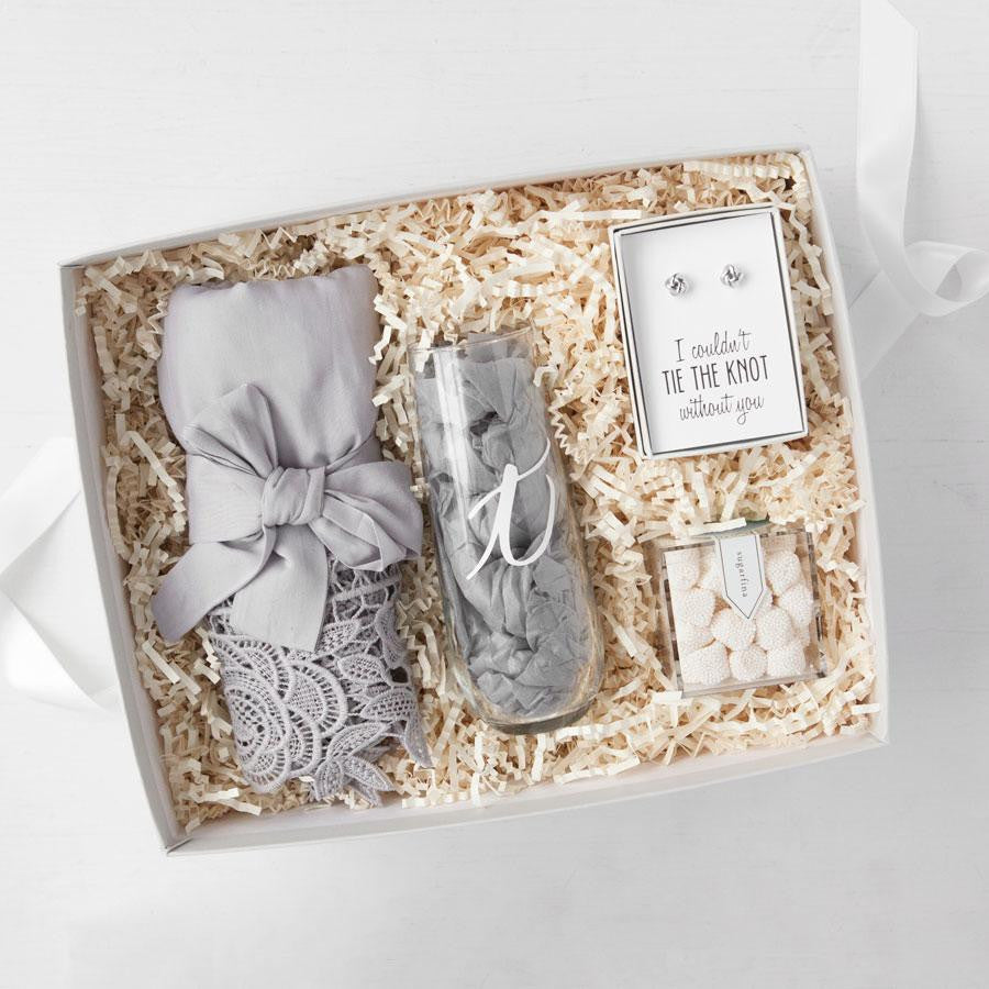 Gray luxe lace trimmed robe rolled with a bow, personalized champagne flute with white "t", I couldn't tie the knot without you set of silver earrings, champagne bubbles candies in clear box. All in white gifting box with ivory paper shred