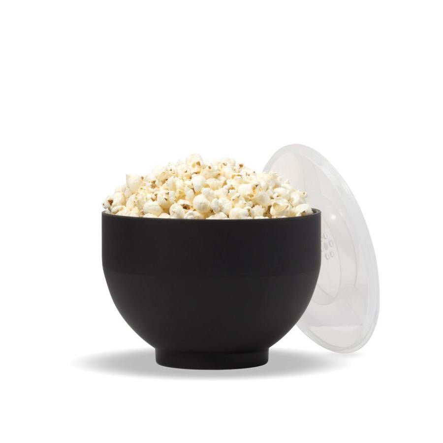 Black silicone popper expanded into bowl holding popcorn with clear plastic lid propped against side. 